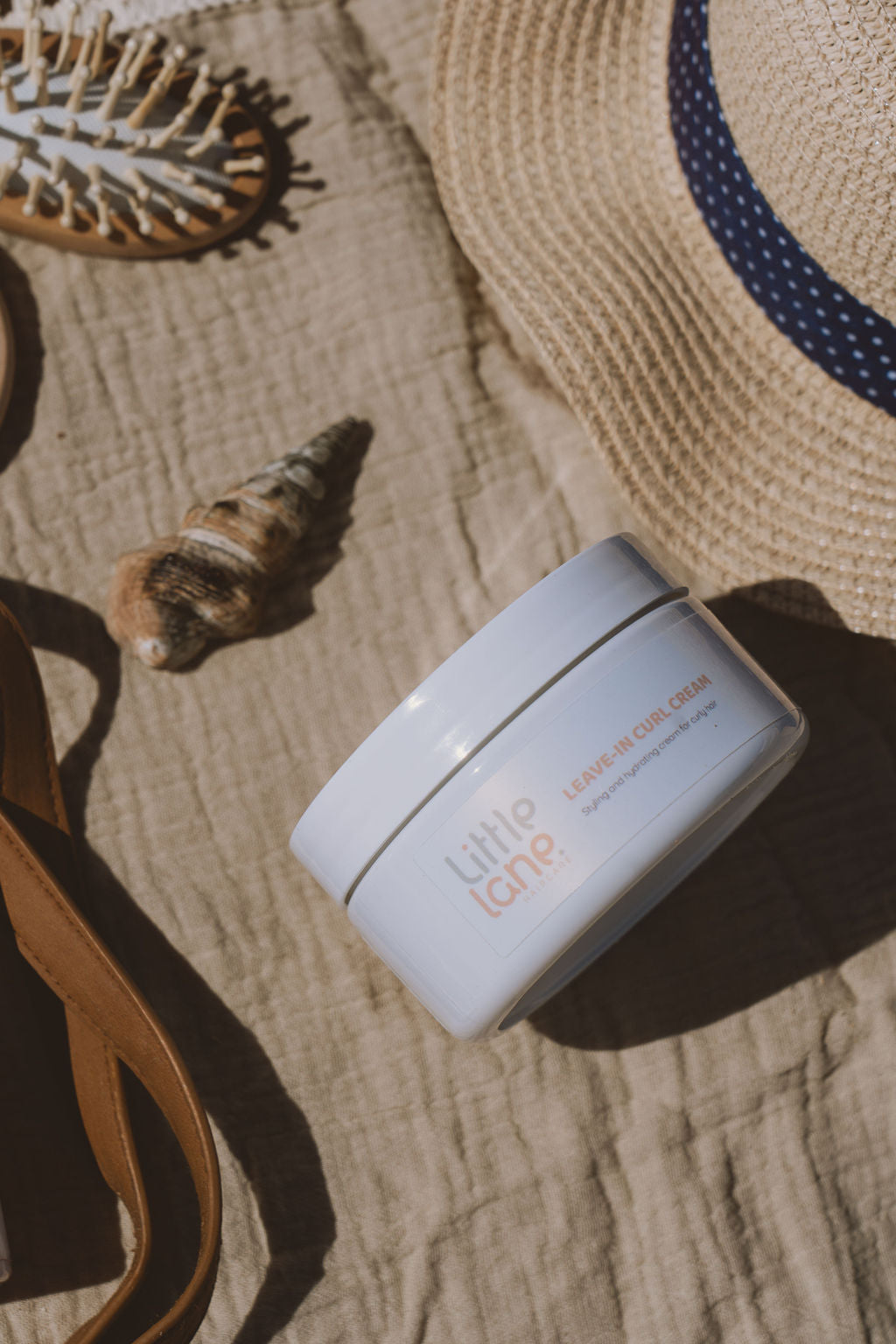 Jar of curl cream with a straw hat and shell on a textured surface