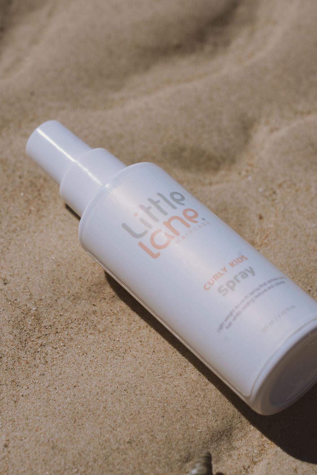 White spray bottle labeled 'little lane' on sandy surface